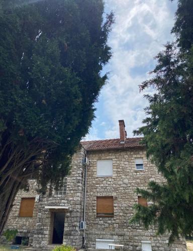 a brick building with windows and trees in front of it at Apartman Bileca in Bileća
