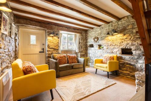 a living room with yellow chairs and a stone wall at Host & Stay - Hutton-le-Hole Cottages in Hutton le Hole