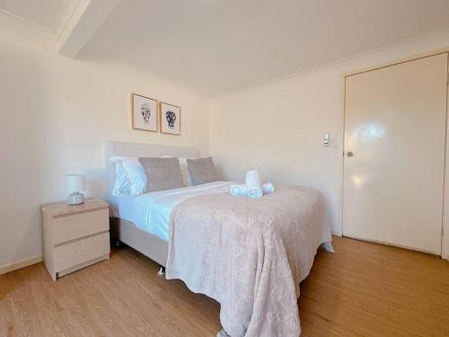 a white bedroom with a bed and a night stand at Comfy unit near Garden City Westfield Street Parking in Brisbane