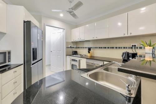 a kitchen with white cabinets and a stainless steel sink at Darwin CBD stunner in Darwin