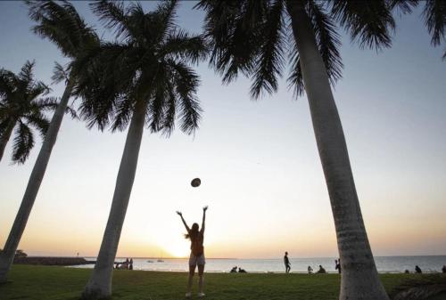 a woman is playing with a ball between two palm trees at Watch the Sun set over Cullen Bay Marina and Harbour in Larrakeyah