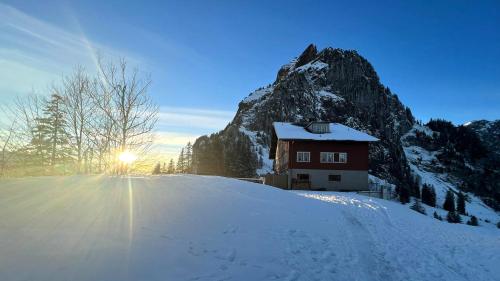a house on a snow covered hill in front of a mountain at Berggasthaus Holzegg - Accessible Only by Cable Car in Alpthal