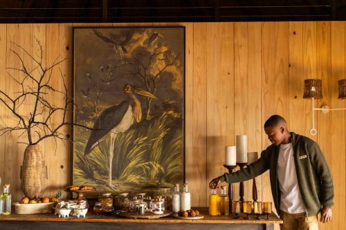 a man standing in front of a table with a painting at Nambiti Hills in Nambiti Private Game Reserve