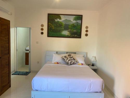 a bedroom with a white bed and a painting on the wall at Manis Guest House in Seminyak