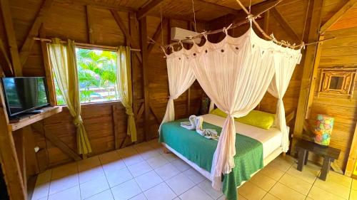 a bedroom with a canopy bed and a television at Gites LES CALEBASSIERS in Deshaies