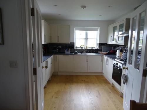 a kitchen with white cabinets and a wooden floor at 3 double bed house with parking in Sheringham in Sheringham