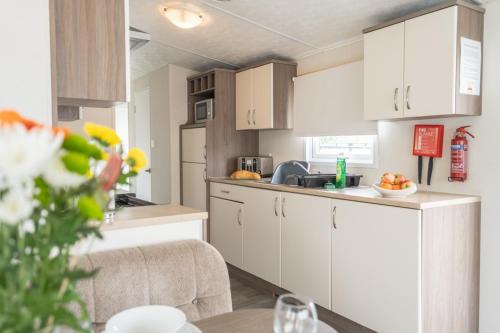 a kitchen with white cabinets and a table with flowers at Marine Holiday Park in Rhyl