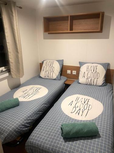 deux lits avec des oreillers « passez une bonne journée » dessus dans l'établissement Mobil-Home neuf Valras-Plage - Camping 4 étoiles les Sables du Midi, à Valras-Plage