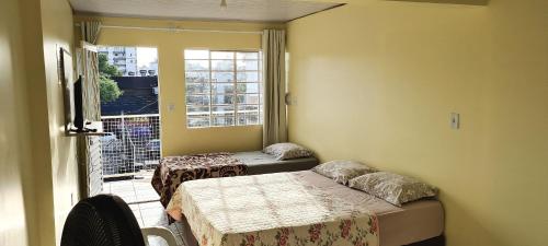 a room with two beds and a table and a window at Loft Confortável no Centro in Chapecó