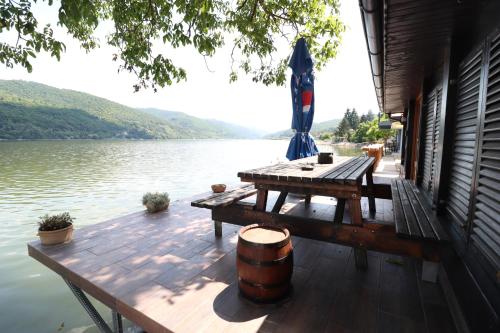 a wooden deck with a table and an umbrella on a lake at Dunavska Vila Milosavljevic in Donji Milanovac