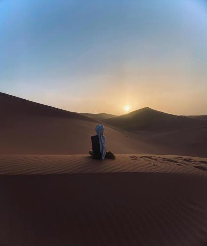 a person sitting in the desert watching the sunset at Riad Dar Fadma in Ouarzazate