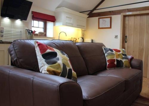 The Granary Thirsk Luxury Holiday Cottage Barn في ثيرسك: أريكة جلدية بنية مع وسادتين عليها
