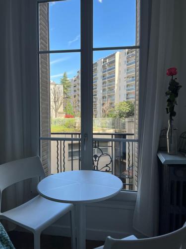 une table blanche et des chaises dans une pièce avec une fenêtre dans l'établissement Joli appartement près de Montmartre, à Paris