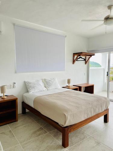 a white bedroom with a bed and a window at Casa A la Mar in Zihuatanejo