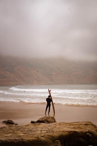 a man standing on a beach with a surfboard at Imsouane surf house in Imsouane