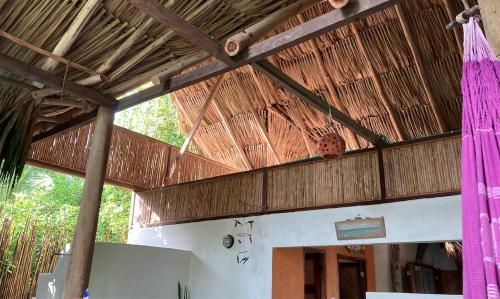 a building with a thatched roof with pink curtains at Casa Monos - Playa y piscina in Guachaca