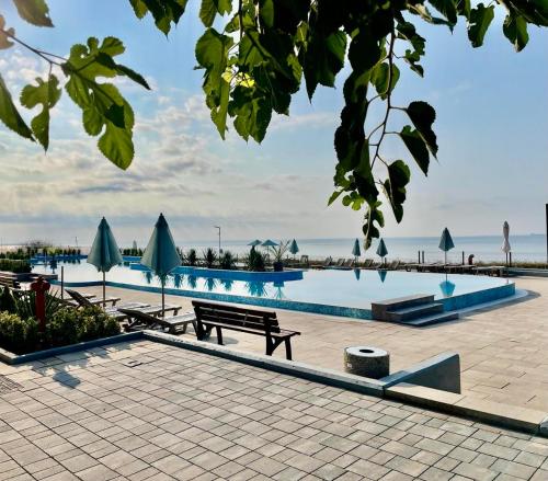 a pool with a bench and tables and umbrellas at Majestic Villas Pomorie Park in Sarafovo