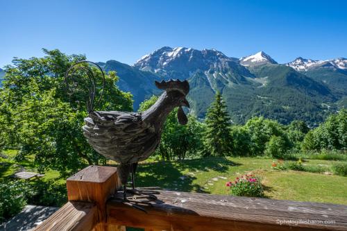 a statue of a chicken on a fence with mountains at Chalet la Forestière in Orcières