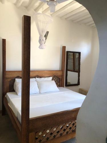 a bedroom with a bed with white sheets and a mirror at Gecko House in Jambiani
