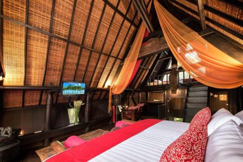 a bedroom with a bed and a tv in a room at Batak Legacy, A Jungle Hideaway in Tabanan