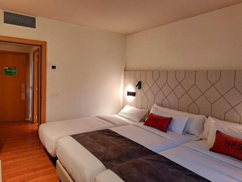 a bedroom with a large bed with white sheets and red pillows at Hotel Puerta Santander in Santander