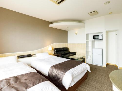 a hotel room with two beds and a chair at Beppu Kanko Hotel Ace in Beppu
