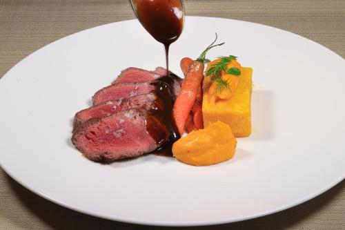 a white plate with a steak and carrots and sauce at Hotel Lago Maggiore - Welcome! in Locarno