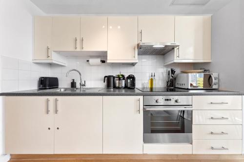 a white kitchen with white cabinets and appliances at Canary Wharf Apartment in London