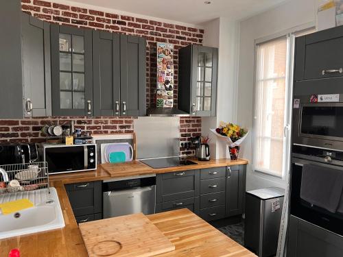 une cuisine avec des armoires noires et un mur en briques dans l'établissement Maison individuelle et cosy, à Houilles