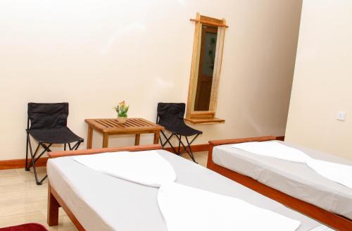 two beds in a room with chairs and a table at Hotel Nilketha Yala Tissamaharama in Tissamaharama