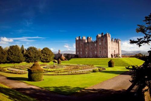 a large castle with a green lawn and a building at Cairndale Hotel & Spa in Dumfries