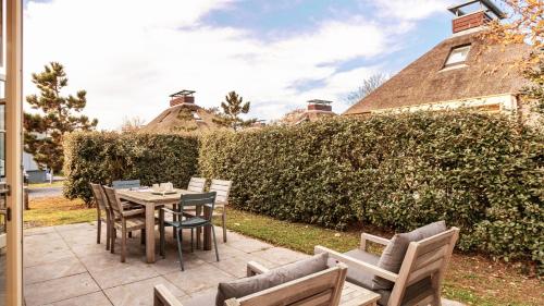 a patio with a table and chairs and a hedge at OUD Duynvallei in Schoorl