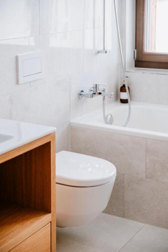 a white bathroom with a toilet and a bath tub at Am Heimberg Skilift - Mullers x Kandahar Suite in Parpan