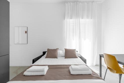 a white bedroom with a bed and a yellow chair at MI CASA - Appartamento in Ponte Nuovo in Milan