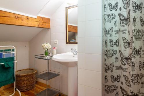 La salle de bains est pourvue d'un lavabo et d'un rideau de douche avec des papillons. dans l'établissement Gîte Gîte Les Combettes 2/3 personnes, à Ispagnac