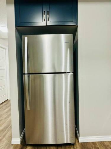 a stainless steel refrigerator in a kitchen with blue cabinets at Parkside Luxury Stay with Xbox Entertainment in Calgary