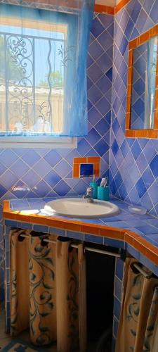 La salle de bains est pourvue de carrelage bleu, d'un lavabo et d'une fenêtre. dans l'établissement Les heures douces, à Régusse