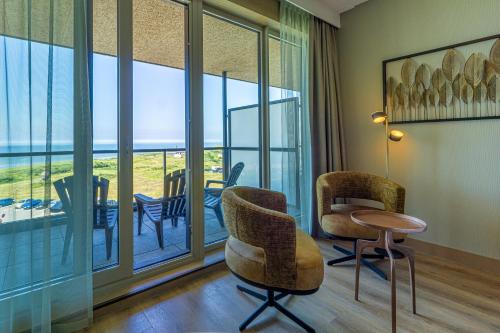 a room with chairs and a table and windows at Strandhotel Het Hoge Duin in Wijk aan Zee