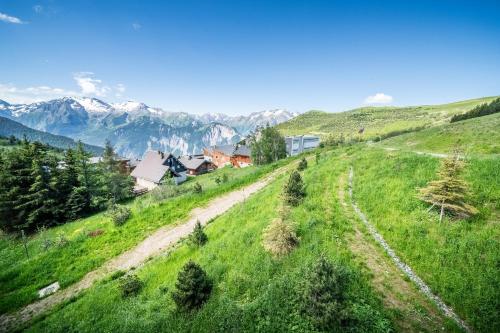 a green grassy hill with mountains in the background at Residence Hameau de Clotaire Alpe d'Huez - by EMERALD STAY in L'Alpe-d'Huez