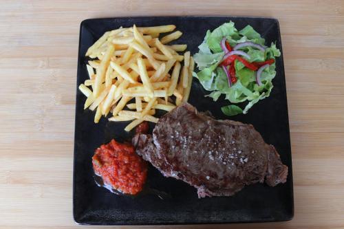 a black plate with steak and french fries and salad at Hotel Mendy in Saint-Jean-le-Vieux