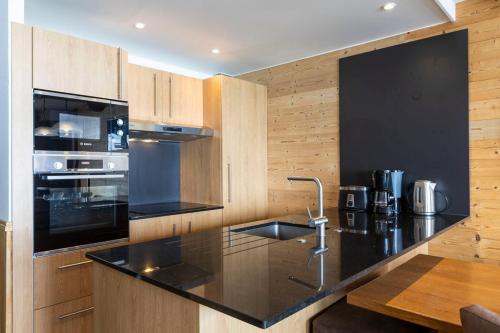 a kitchen with a black counter top and wooden cabinets at Résidence Les Balcons de Val Thorens & Spa in Val Thorens