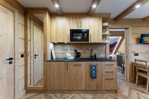 een keuken met houten kasten, een wastafel en een magnetron bij Nowy Szlak Luksusowe Apartamenty in Kościelisko