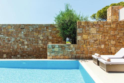 a swimming pool with two lounge chairs and a brick wall at Ikos Olivia in Gerakini