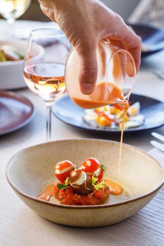 a person pouring sauce into a bowl of food at Ikos Aria in Kefalos