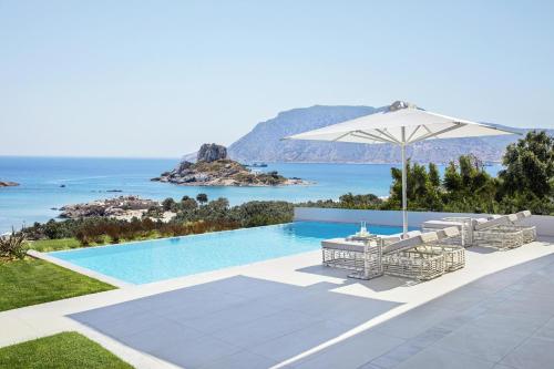 a swimming pool with chairs and an umbrella and the ocean at Ikos Aria in Kefalos