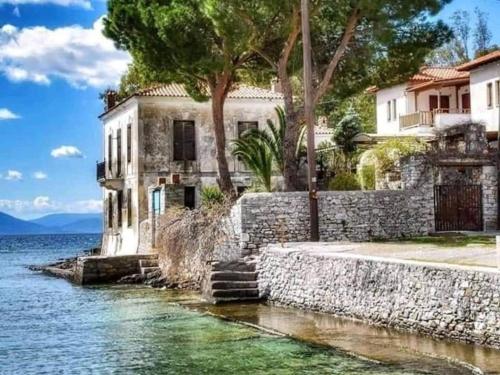 an old house on the water next to a stone wall at Orsiida Seaside Cottage KGatzea in Kato Gatzea