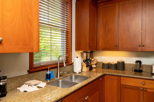 a kitchen with wooden cabinets and a sink at Hilton Pool Pass Included, Kolea - Stylish & Comfy Walk to Beach Patio Pool Gym in Waikoloa