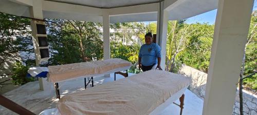 a man standing on a porch with two beds at Tu Departamento en Mahahual in Mahahual