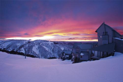 a building in the snow with a sunset in the background at Red Robin in Mount Hotham