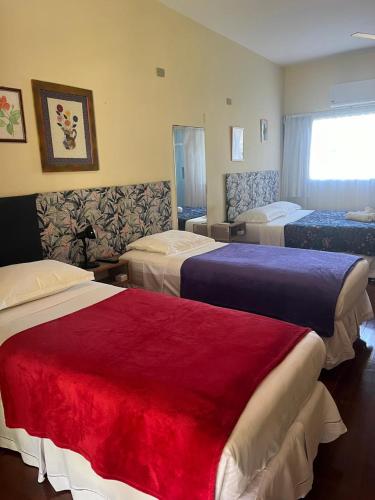 a hotel room with three beds and a red blanket at Hospedagem Praia de Piratininga in Niterói